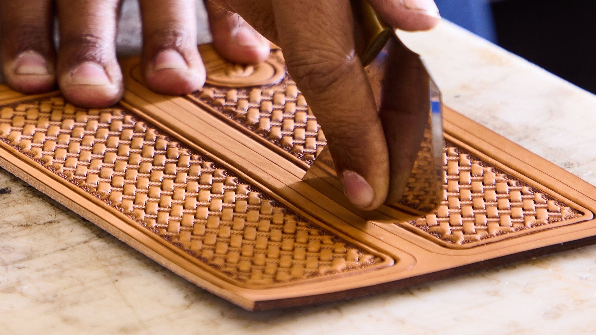 Person working on a leather product with intricate patterns on a marble surface